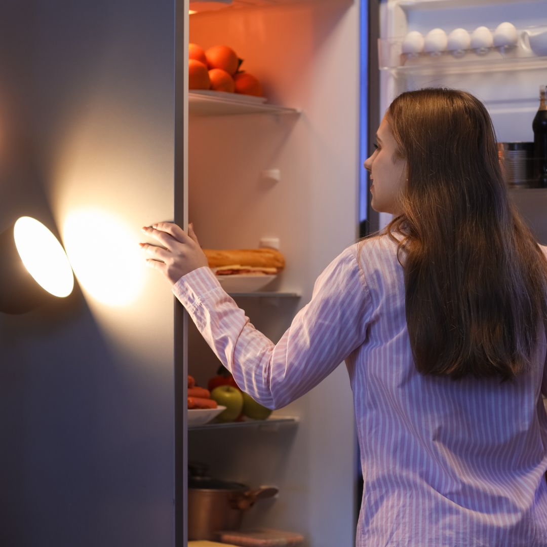 Woman with PMOS looking into a kitchen cupboard mid-morning, illustrating constant hunger and appetite regulation.